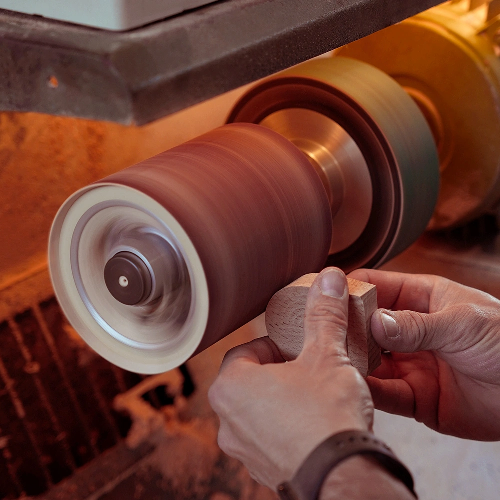 Una persona utilizza un tornio elettrico per modellare un pezzo di legno, tenendolo fermo con entrambe le mani mentre la macchina gira rapidamente, creando segatura in un'officina.