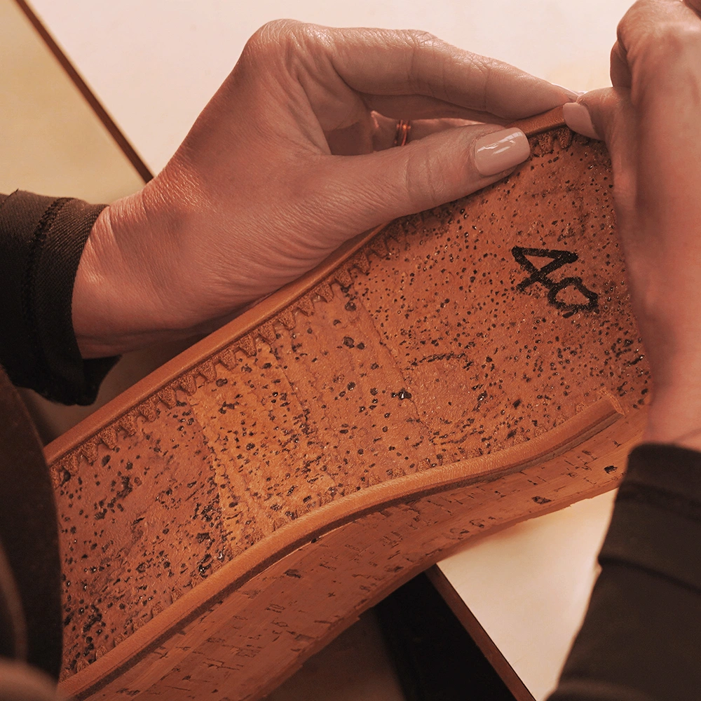 Primo piano di mani che cuciono con cura il bordo di una suola di sughero, contrassegnata dal numero 40, su un tavolo da lavoro.