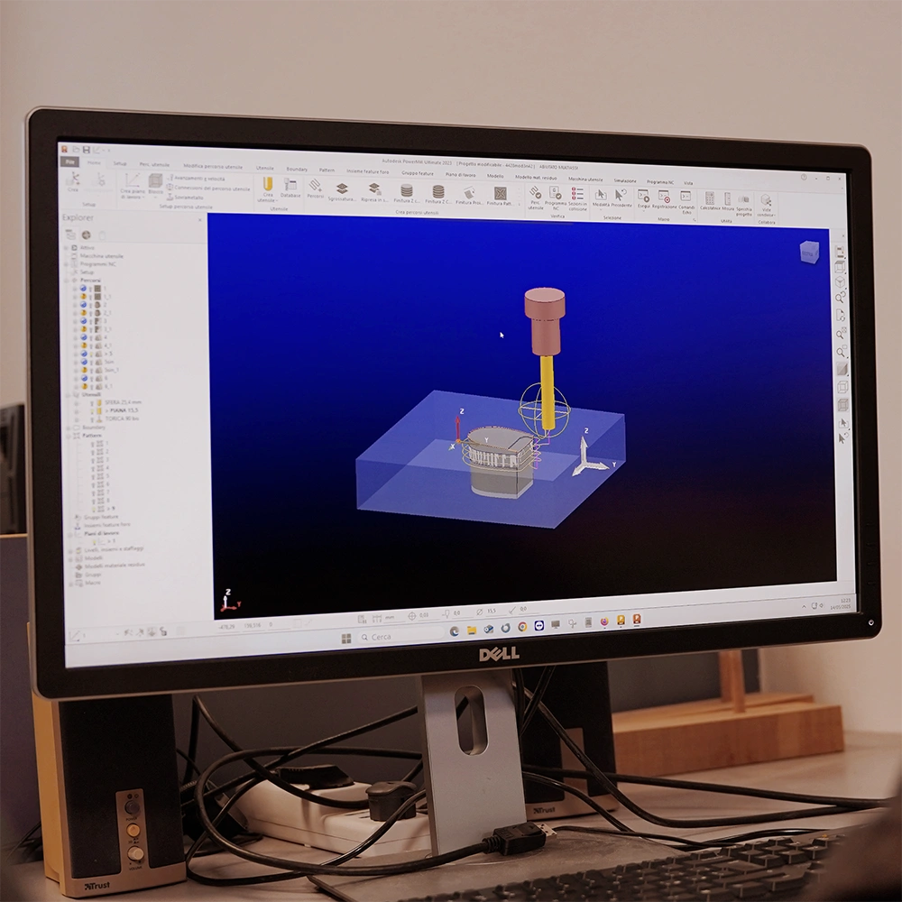 Un monitor Dell visualizza un software di modellazione 3D con simulazione di ingranaggi e strumenti in un'area di lavoro blu, circondata da icone e barre degli strumenti. Sotto lo schermo sono visibili i cavi e la tastiera.